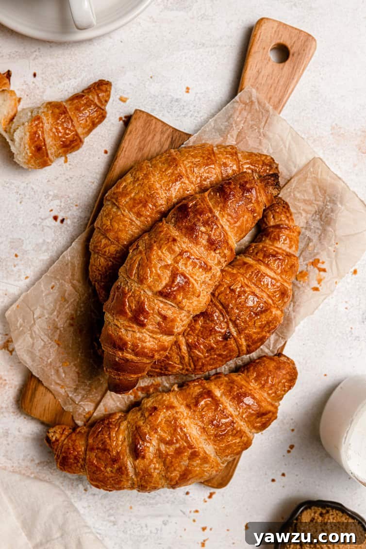A beautiful pile of golden-brown homemade croissants resting on a rustic wooden cutting board, showcasing their inviting texture and crisp crust.