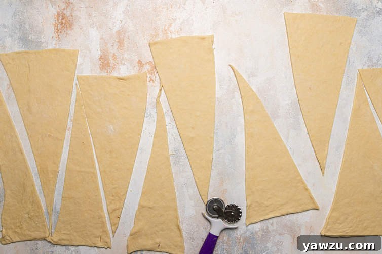 Croissant dough expertly rolled out into a large rectangle and precisely cut into uniform triangles, prepared for the shaping process.