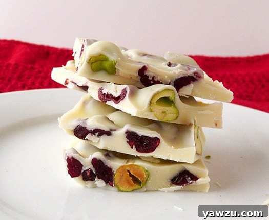 Stack of 4 pieces of pistachio and cranberry white chocolate bark on a white plate, showcasing its vibrant red and green colors.