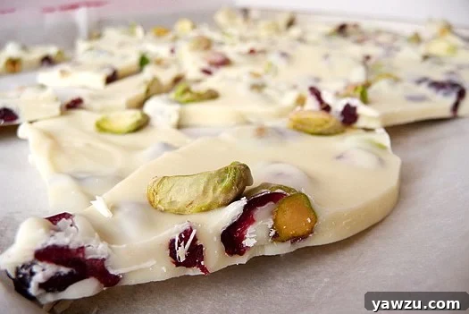 Pistachio and cranberry white chocolate bark spread evenly on a parchment-lined baking sheet before being broken into pieces.
