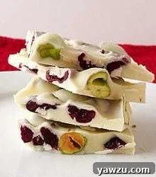 Stack of 4 pieces of pistachio and cranberry white chocolate bark on a white plate, showcasing its beautiful textures and colors.