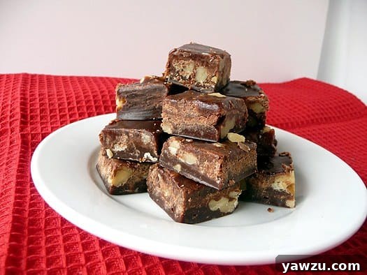 Stacked squares of rich chocolate walnut fudge on a pristine white plate, inviting a taste.