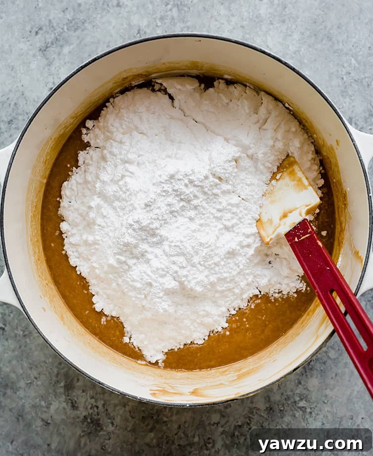 Melted butter and peanut butter in a pot with powdered sugar being mixed in until smooth, a key step for creamy fudge.